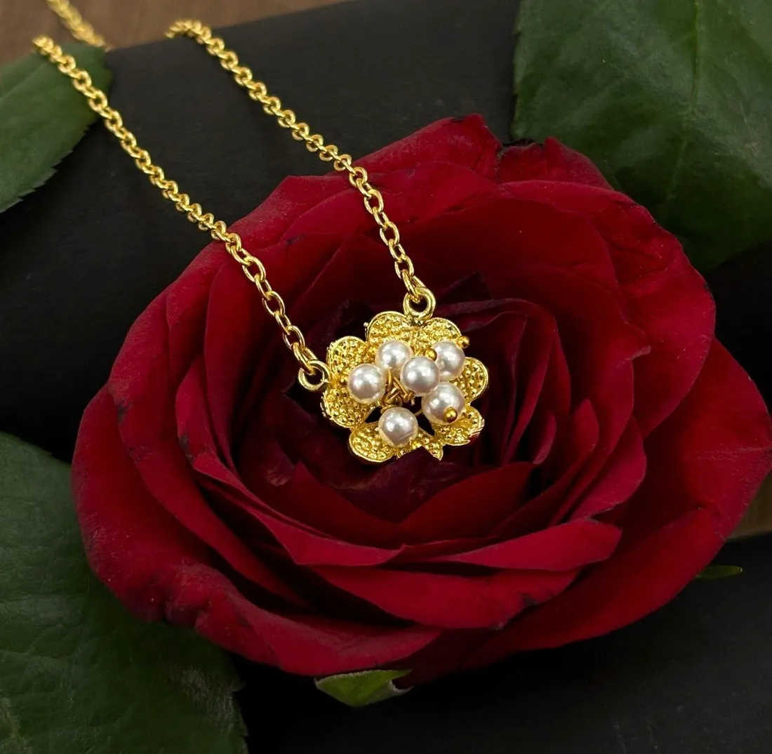 An anti-tarnish gold-tone chain with a pearl flower pendant resting on a fresh red rose, its petals still damp