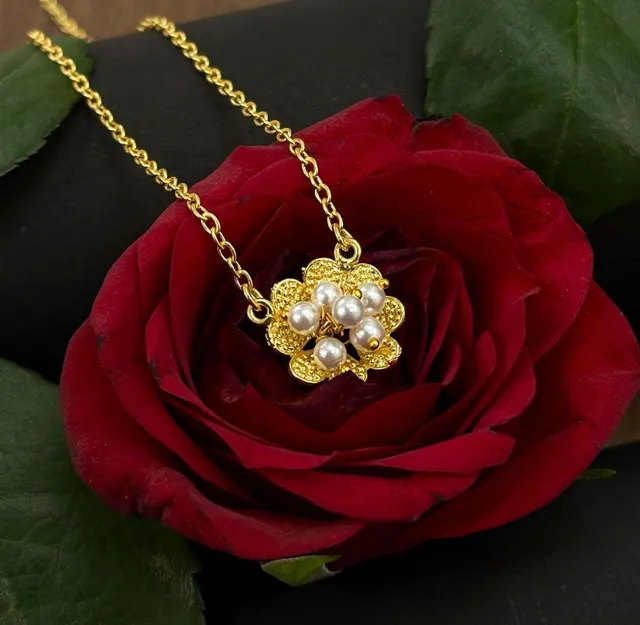 An anti-tarnish gold-tone chain with a pearl flower pendant resting on a fresh red rose, its petals still damp