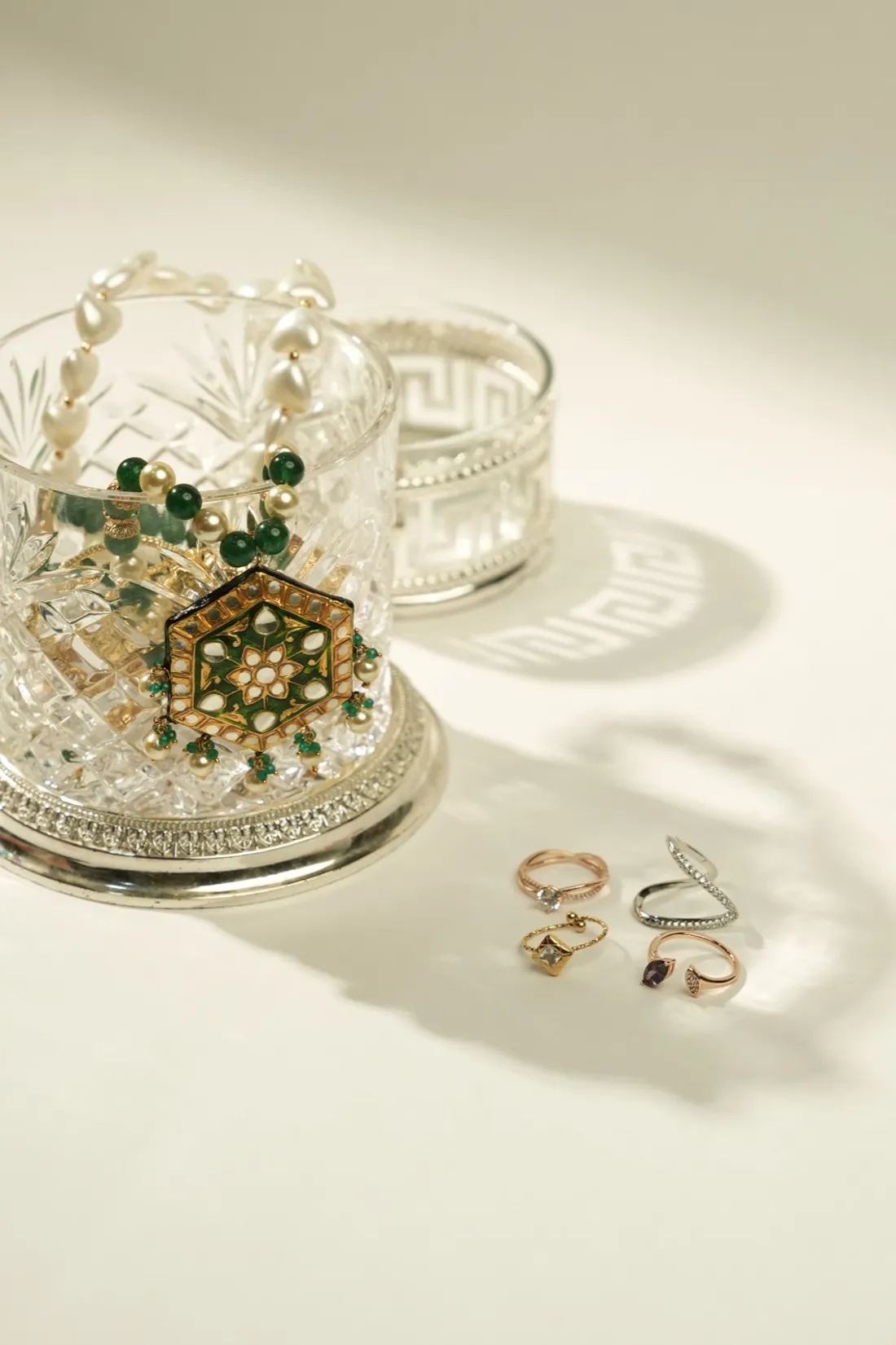Pearl and green-stone jewellery arranged in crystal dishes beside a set of gold rings