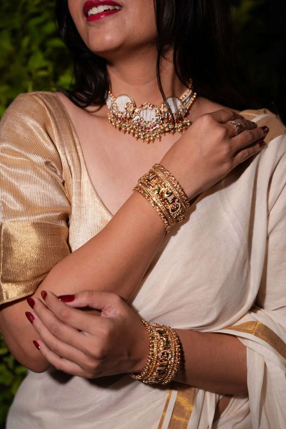 A woman in a cream-and-gold saree wearing a kundan choker and gold bangles