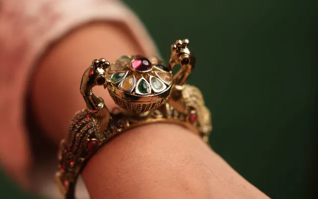 Gold-tone kundan kada bracelet with red and green stones worn on a wrist