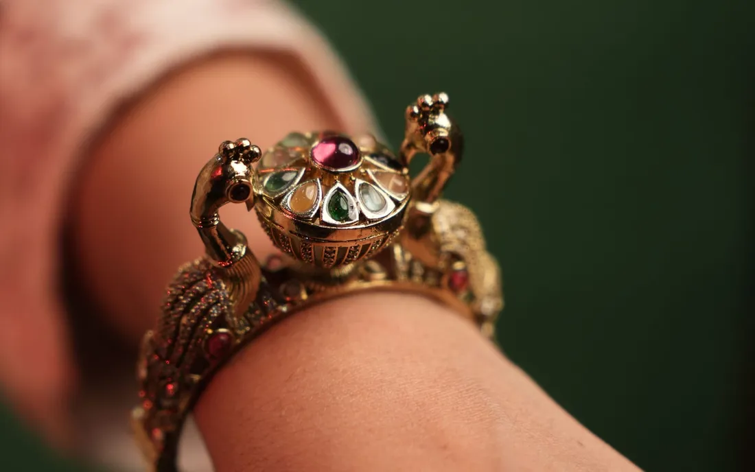 Gold-tone kundan kada bracelet with red and green stones worn on a wrist