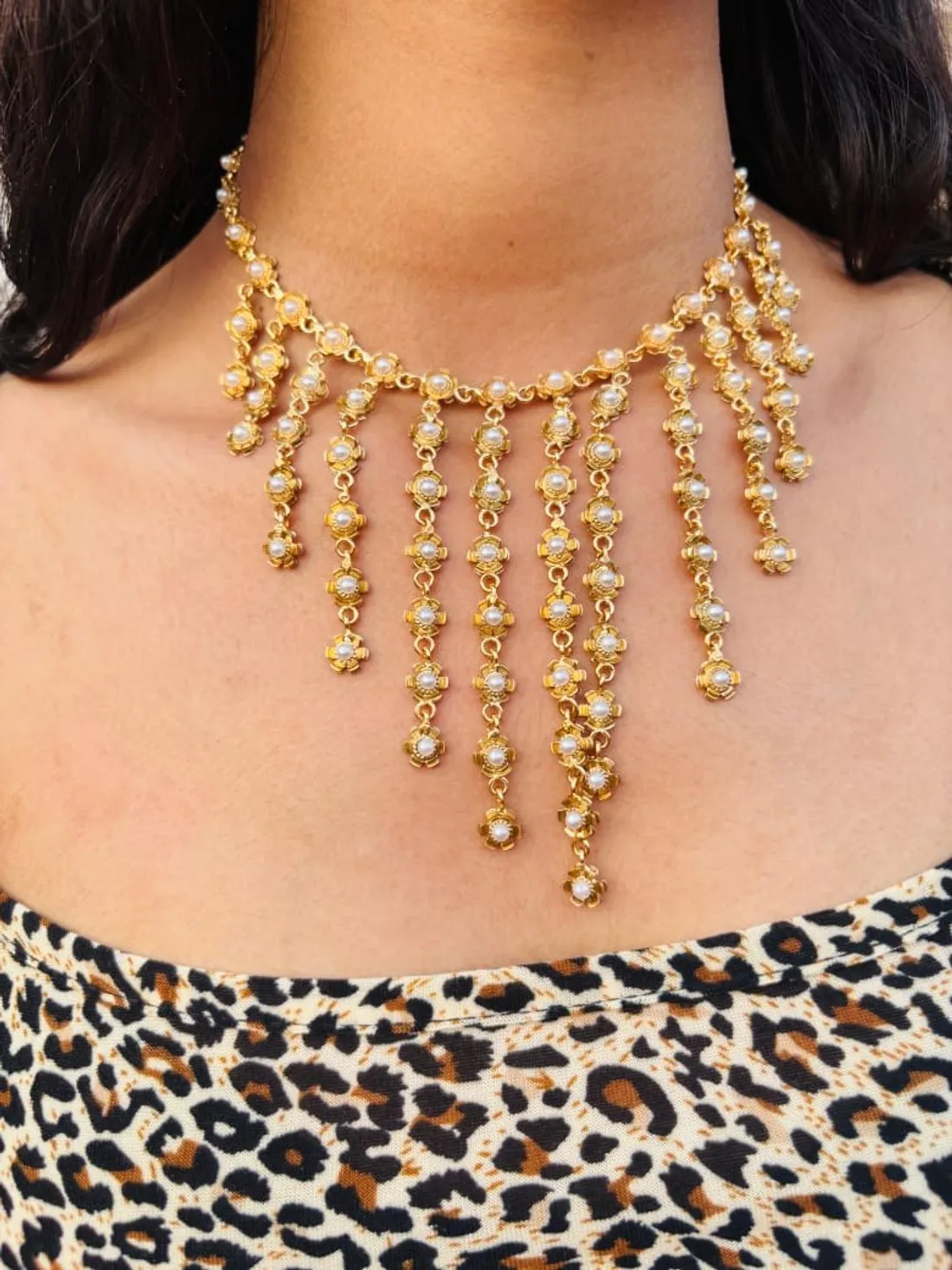 A gold-tone pearl fringe choker worn with a wide boat neckline, showing how the necklace sits above the edge of the neckline