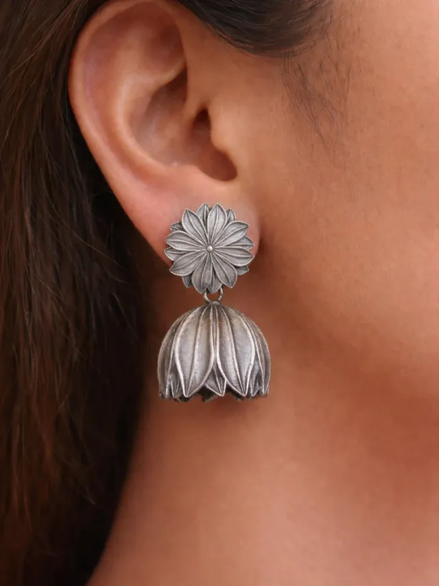 An oxidised silver floral jhumka earring worn on the ear