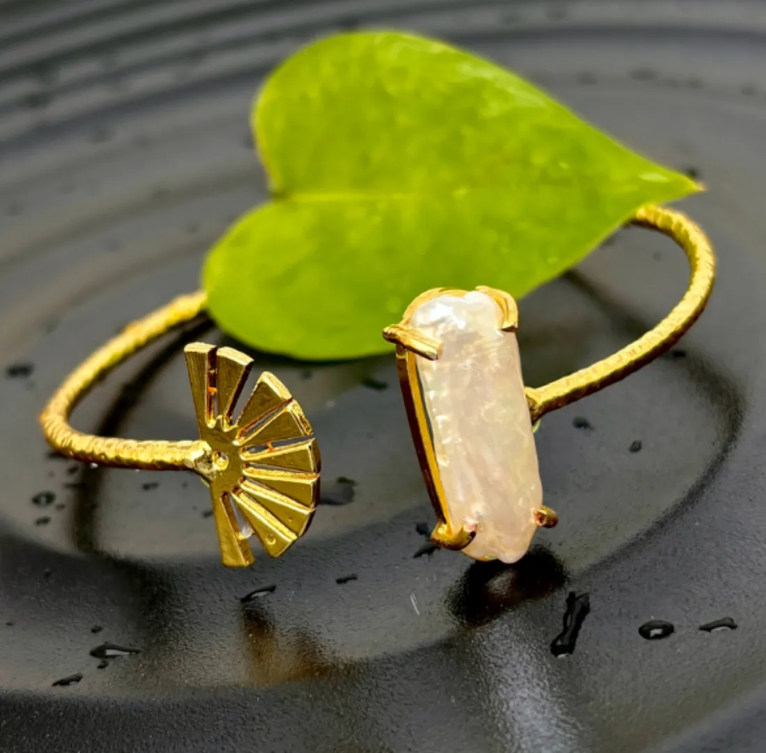 A gold cuff bangle with a pearl and flower motif