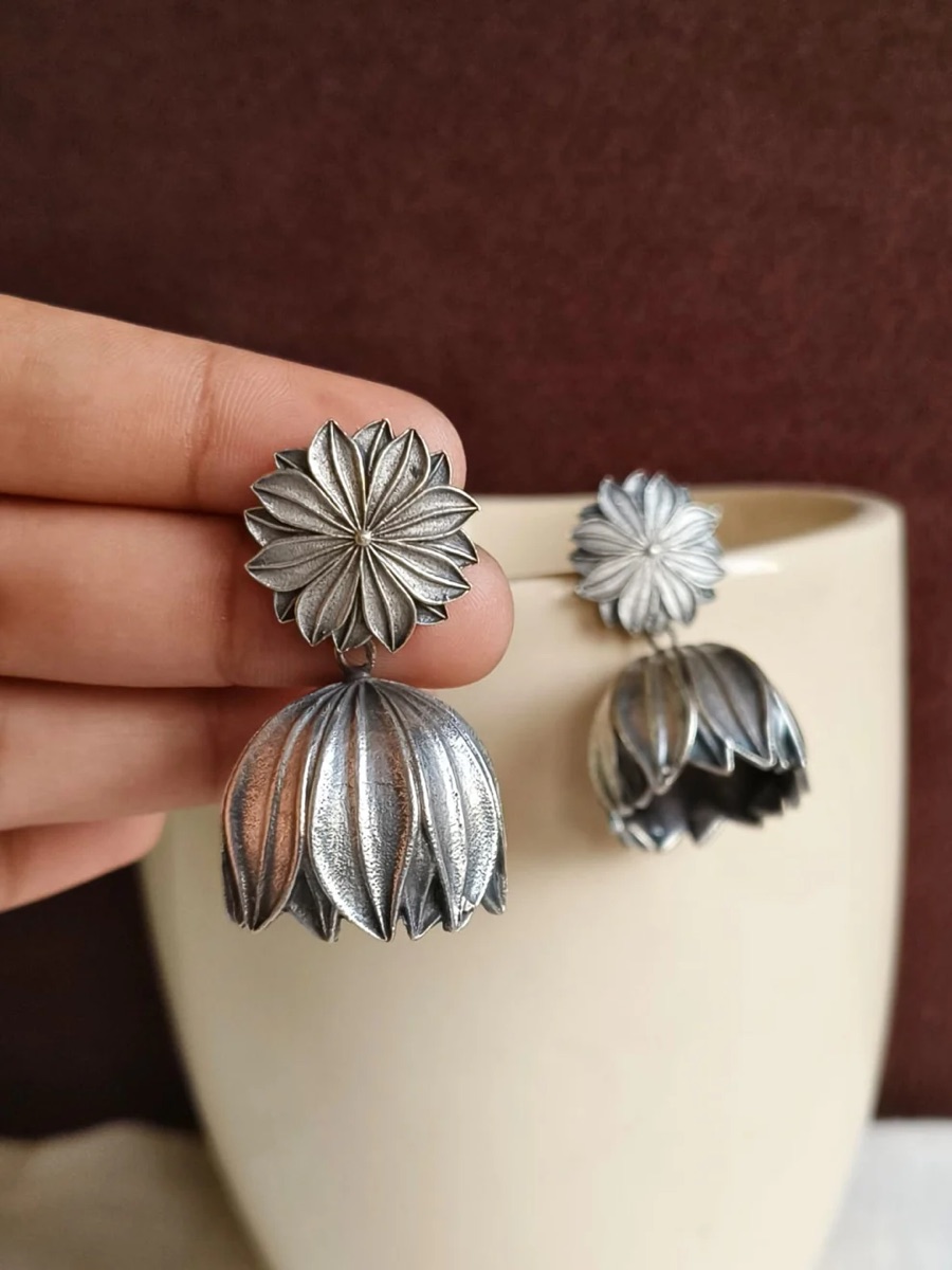An oxidised silver floral jhumka held in hand